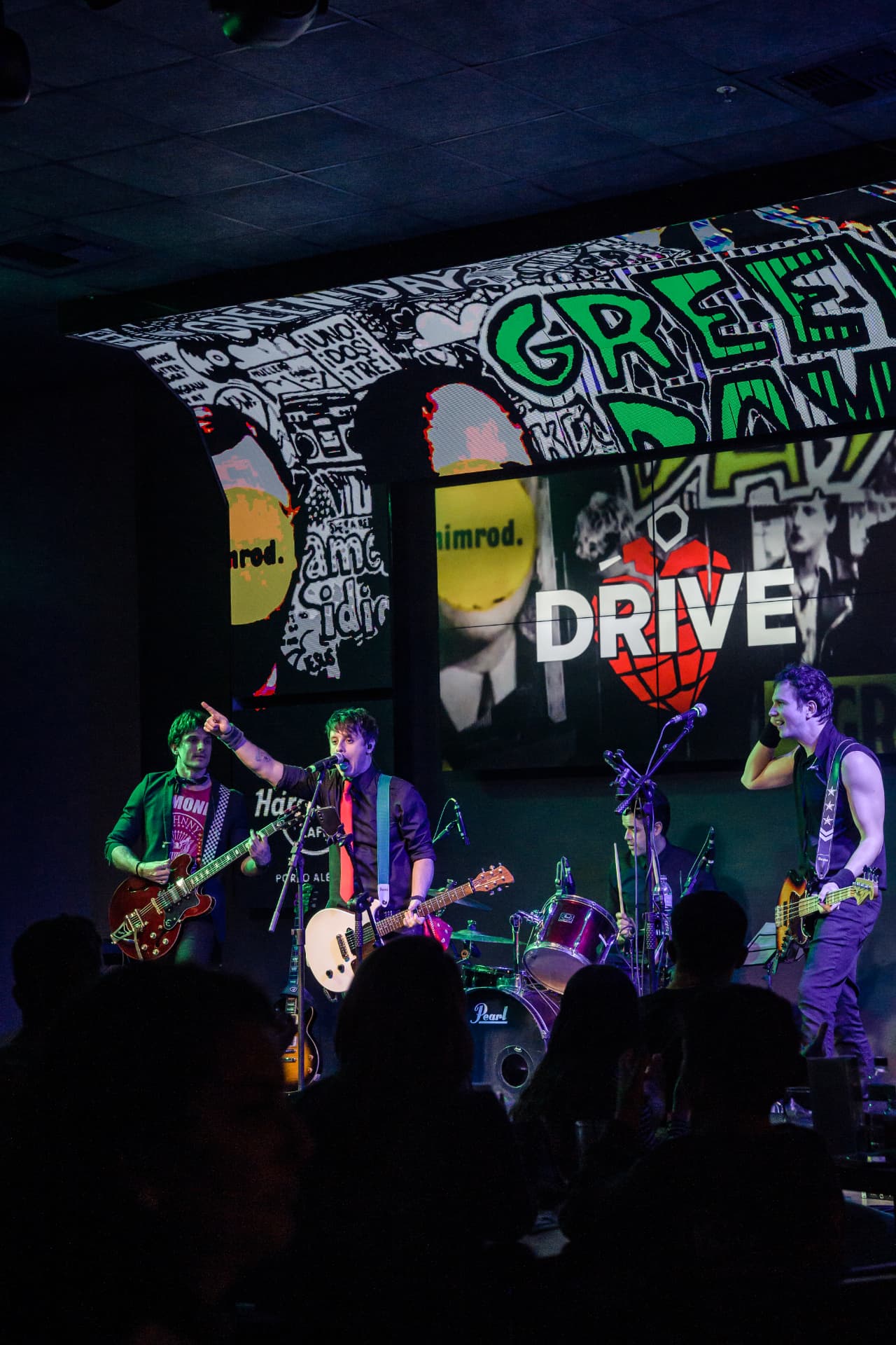 A banda Drive completa no palco com painel do Green Day ao fundo